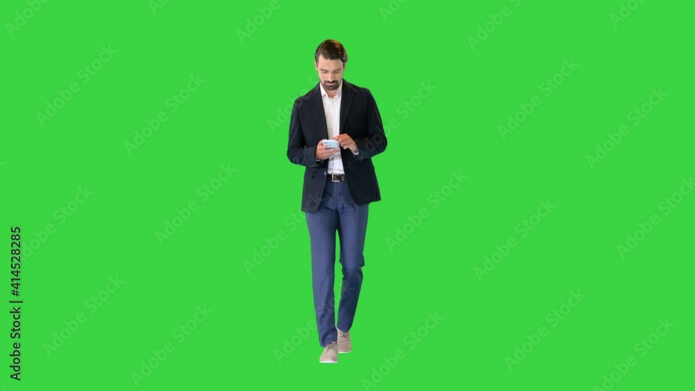 Young businessman walking and texting on his phone on a Green Screen, Chroma Key. Young businessman walking and texting on his phone on a Green Screen, Chroma Key.