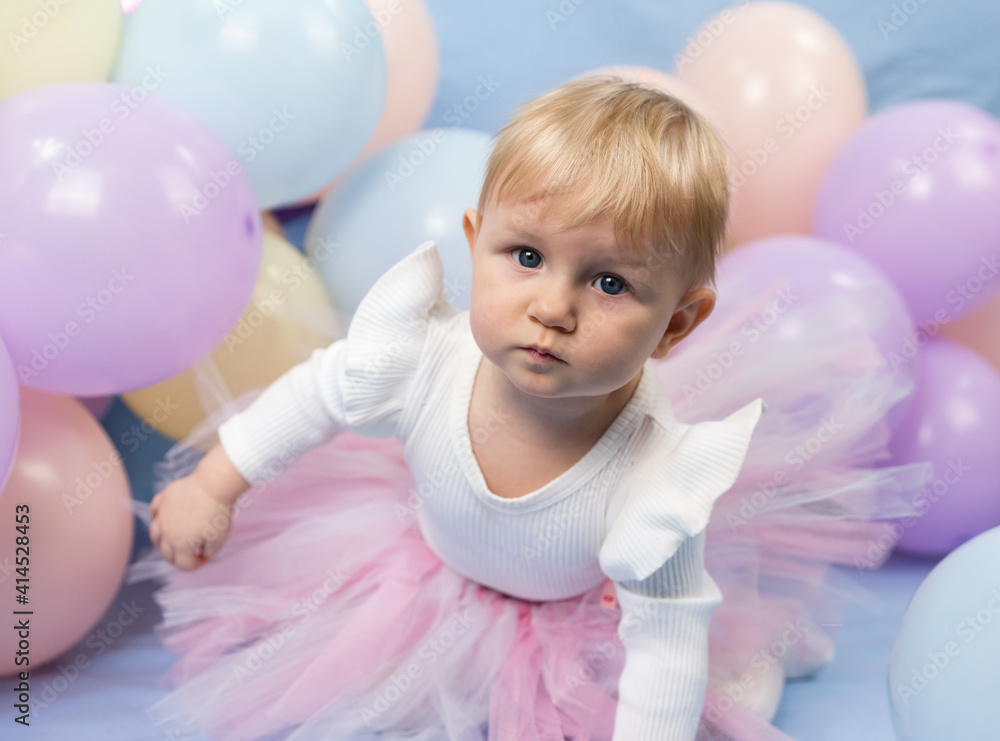A beautiful little girl 1 year old in pink tutu skirt among balloons looks up at the camera A beautiful little girl 1 year old in pink tutu skirt among balloons looks up at the camera
