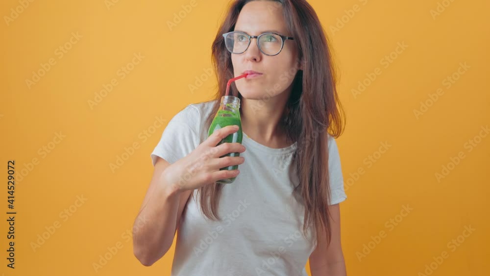Cute child drinks a green smoothie cocktail from a bottle on a yellow background. Little girl holds a glass bottle with a healthy drink of broccoli, kale, spinach, fruits, vegetables. Concept of Cute child drinks a green smoothie cocktail from a bottle on a yellow background. Little girl holds a glass bottle with a healthy drink of broccoli, kale, spinach, fruits, vegetables. Concept of
