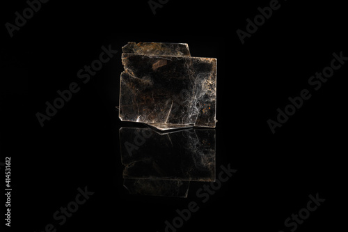 Natural mineral from geological collection - rough muscovite mica, common mica on black glass background. from Poldnevoe, Ural, Russia.