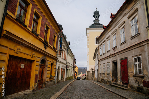 Narrow medieval picturesque street with baroque and renaissance historical buildings in winter day  bell tower of church of St. Nicholas  Bohemian Paradise  Turnov  Czech Republic