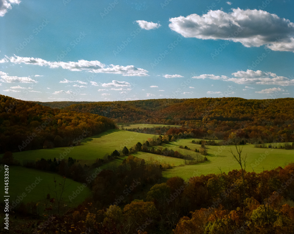 View of an Ozarks meadow in Autumn with leaves beginning to turn and puffy clouds from a ridge above Akers, Missouri  and Current River on Highway K.