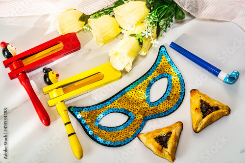 Purim celebration concept. Ratchet, hamantaschen cookies and masquerade mask next to flowers