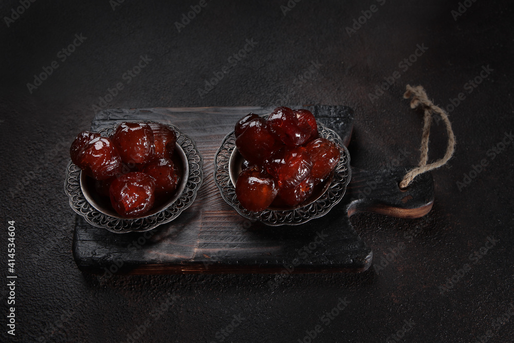 Sweet dessert of dates in sugar transparent glaze on a wooden board on a dark background. Top view. Sweet dessert of dates in sugar transparent glaze on a wooden board on a dark background. Top view.
