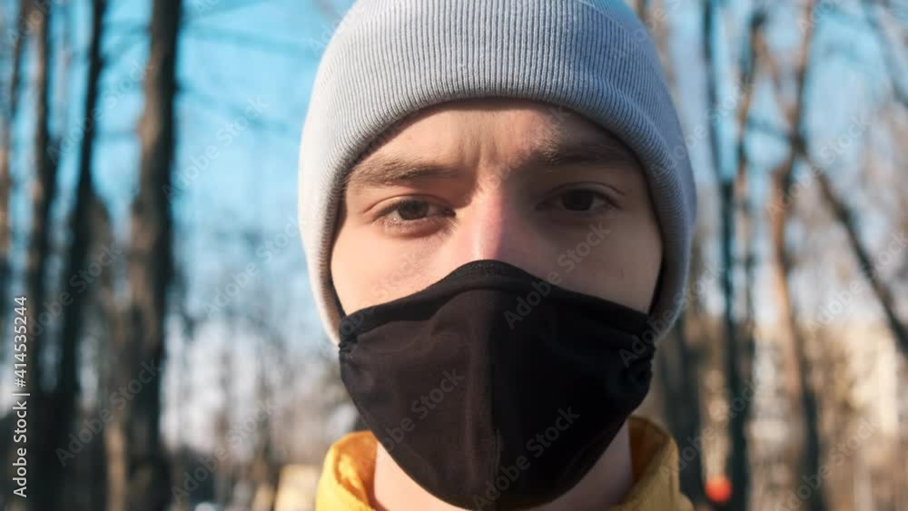 Food delivery man on a scooter in a park, zipping up his jacket and looking into camera. Black medical mask. Winter Food delivery man on a scooter in a park, zipping up his jacket and looking into camera. Black medical mask. Winter