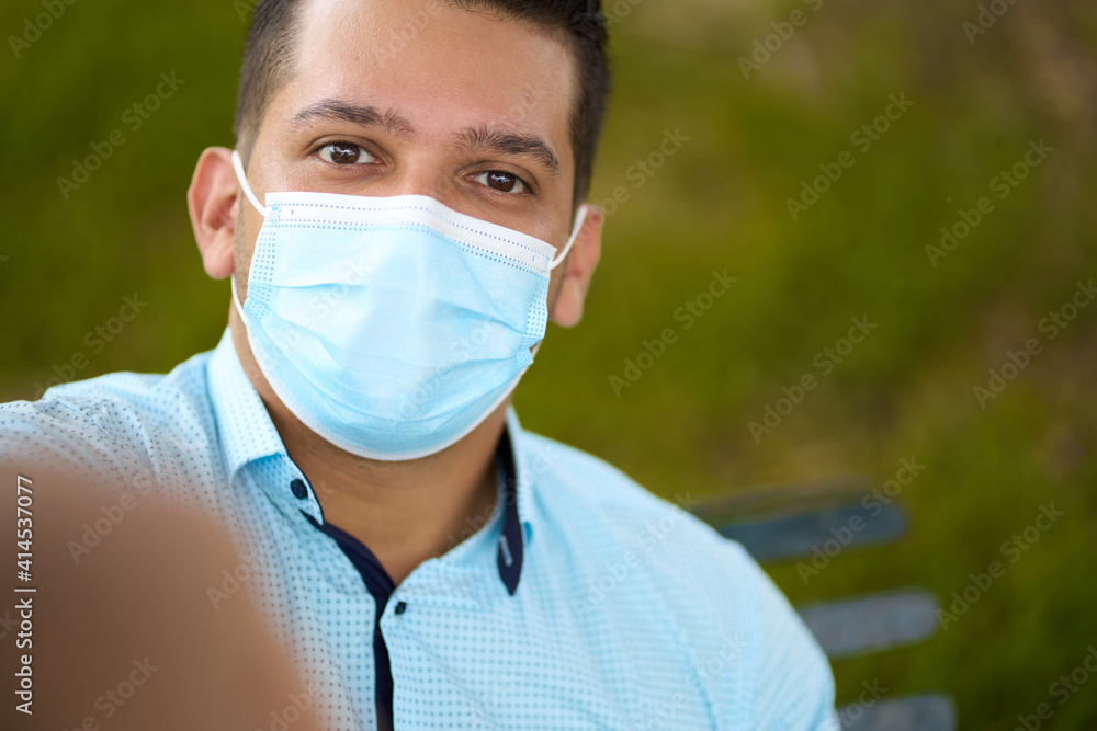 portrait of a handsome young ecuadorian taking a selfie, wearing a facemask, sitting on a park bench, in the city of guayaquil portrait of a handsome young ecuadorian taking a selfie, wearing a facemask, sitting on a park bench, in the city of guayaquil