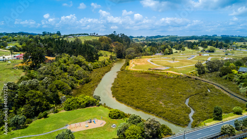 Aerial view of a small river running to the sea through green countryside spotted with little farms. Auckland, New Zealand.