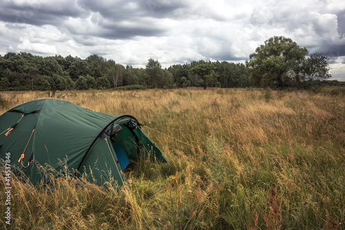 Camping tent on summer rural field in overcast day with dramatic sky with forest on background during camping holidays