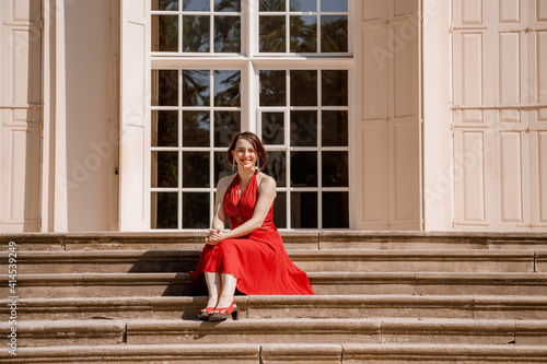 The Great Orangery a classicistic orangery in Lazienki Krolewskie park in Warsaw, Poland. Woman Outdoor Beauty Portrait. A woman with red dress sitting Stairs. photo