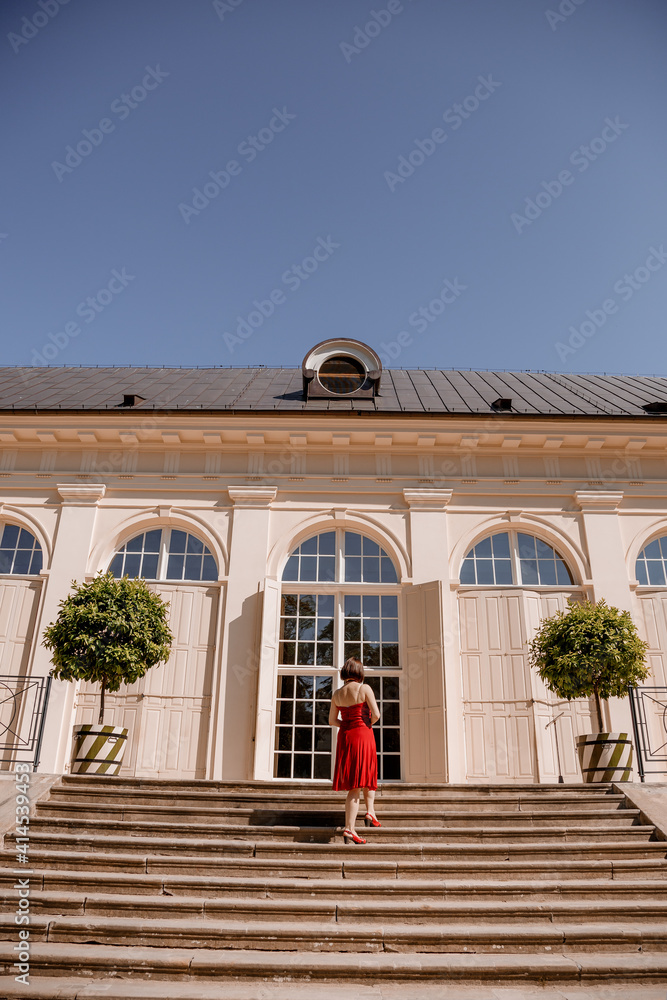 The Great Orangery a classicistic orangery in Lazienki Krolewskie park in Warsaw, Poland. Woman Outdoor Beauty Portrait. A woman with red dress sitting Stairs.
