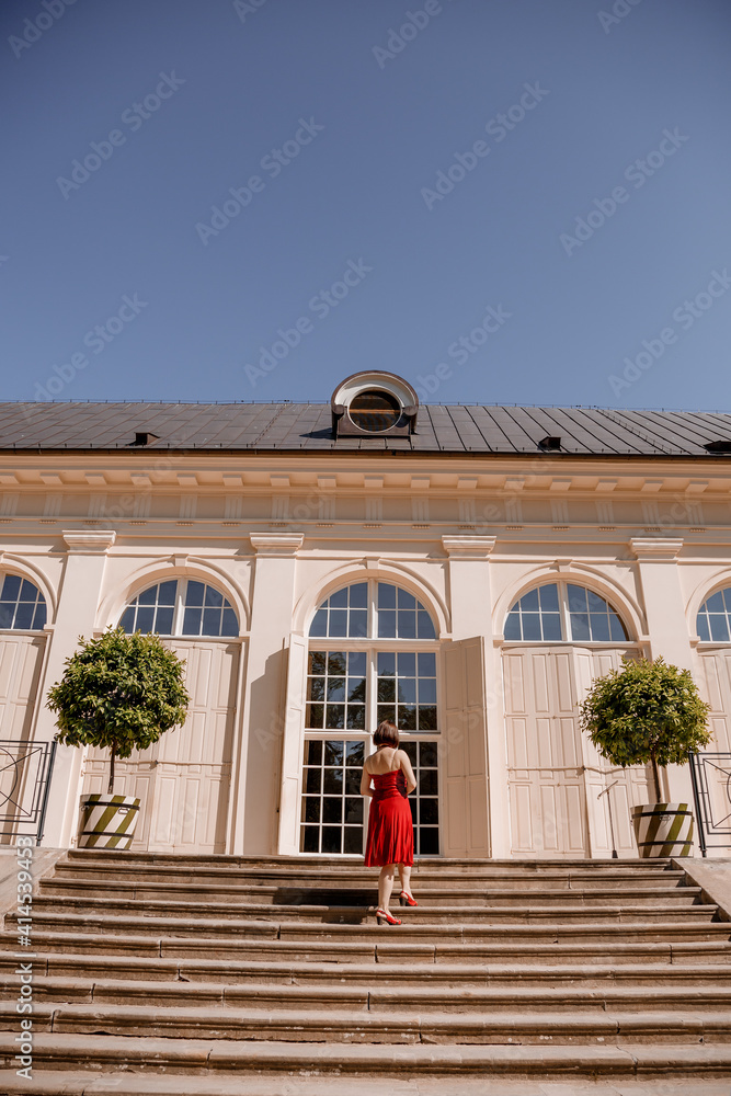 The Great Orangery a classicistic orangery in Lazienki Krolewskie park in Warsaw, Poland. Woman Outdoor Beauty Portrait. A woman with red dress sitting Stairs. The Great Orangery a classicistic orangery in Lazienki Krolewskie park in Warsaw, Poland. Woman Outdoor Beauty Portrait. A woman with red dress sitting Stairs.