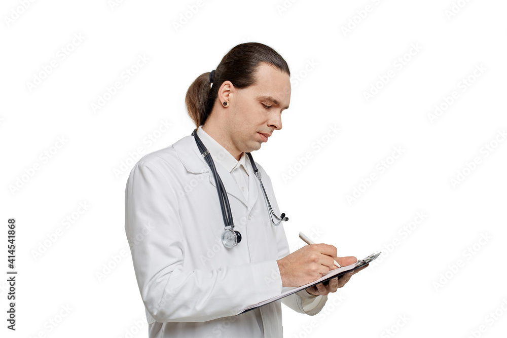 A young handsome male doctor writes with a writing pen on paper in a tablet. White isolated background. A young handsome male doctor writes with a writing pen on paper in a tablet. White isolated background.