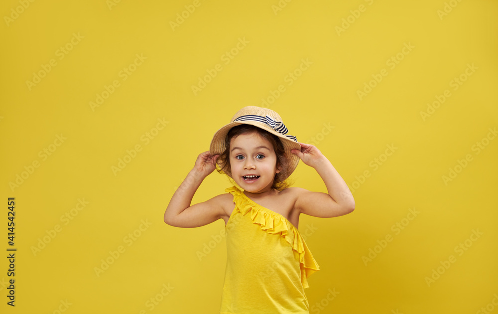 Beautiful little girl wearing summer hat poses on a yellow background with copy space expressing emotion, surprise Beautiful little girl wearing summer hat poses on a yellow background with copy space expressing emotion, surprise