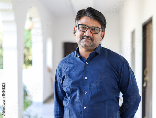 Portrait of a middle-aged Indian male with eyeglasses wearing a blue shirt