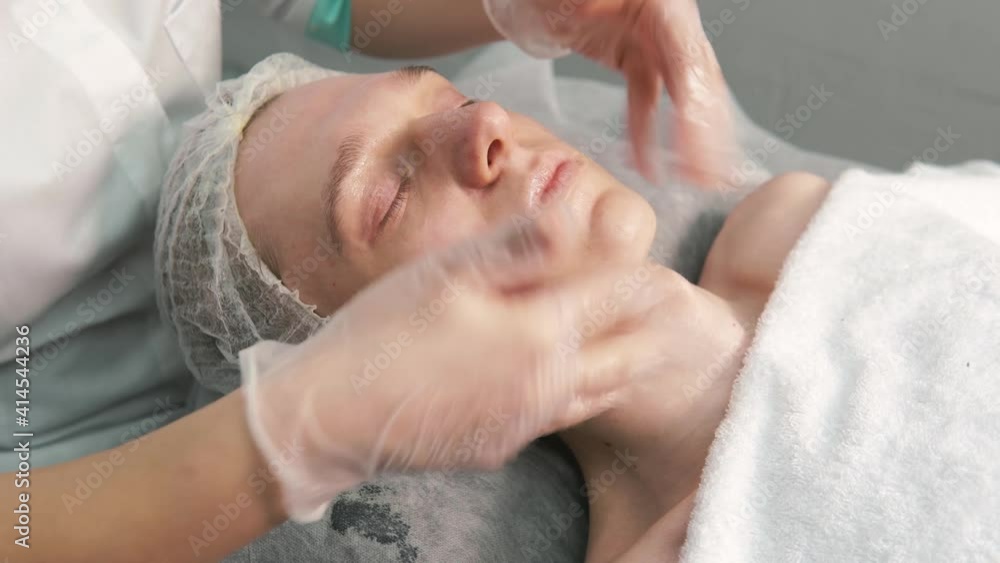 The cosmetologist applies a gel to the face and does a facial massage. Women's hands in gloves. A man takes care of the skin of the face. The cosmetologist applies a gel to the face and does a facial massage. Women's hands in gloves. A man takes care of the skin of the face.