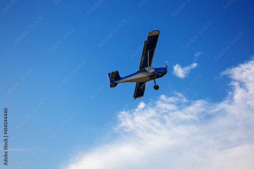 Small private plane climbs through the clouds. Fliyng ultralight aircraft across the blue sky. Copy space.