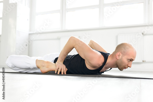 Fototapeta Naklejka Na Ścianę i Meble -  man working out, doing Frog Yin Yoga Pose, Mandukasana posture in class on fitness mat. sport, stretching, yoga concept