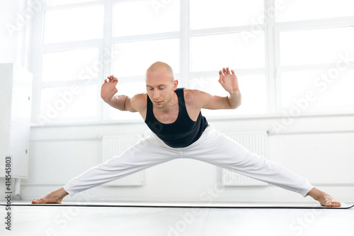 healthy male stretching, doing hard yoga exercises alone in studio on fitness mat, engaged in healthy lifestyle. sport concept