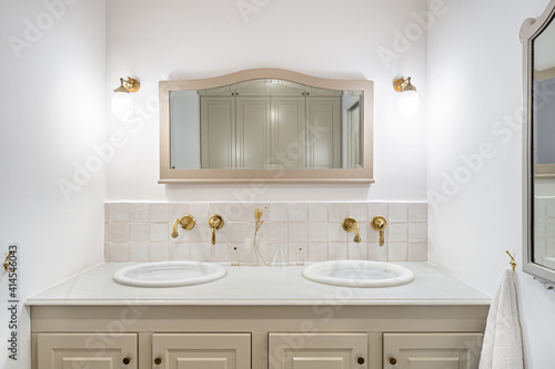 Interior of retro or classic style bathroom decorated in beige color with two sinks  golden faucets and vintage mirror.