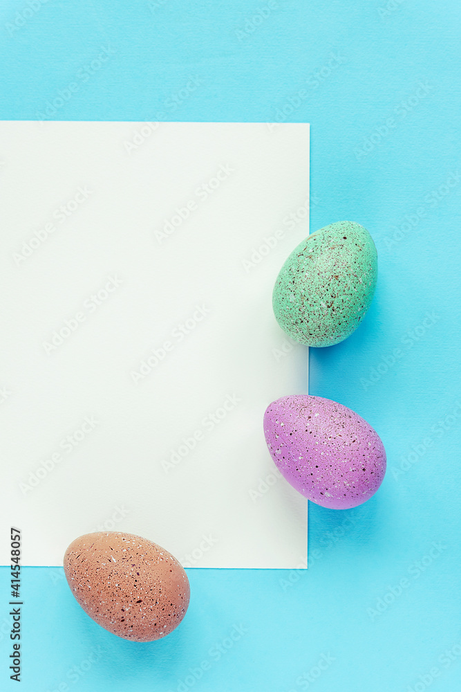 Fototapeta premium Three painted eggs and blank sheet on blue background, top view, flat lay