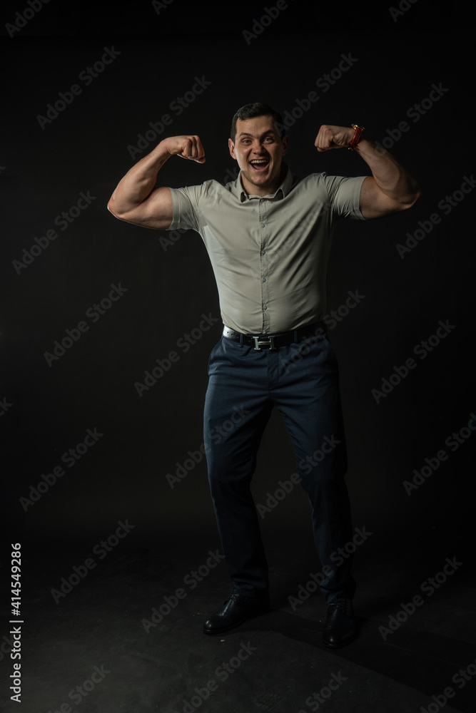 Shows off muscle and smiling bodybuilder in grey shirt on black background confident elegance model, portrait modern suit, studio beautiful. Content boy, shirt cool black Shows off muscle and smiling bodybuilder in grey shirt on black background confident elegance model, portrait modern suit, studio beautiful. Content boy, shirt cool black