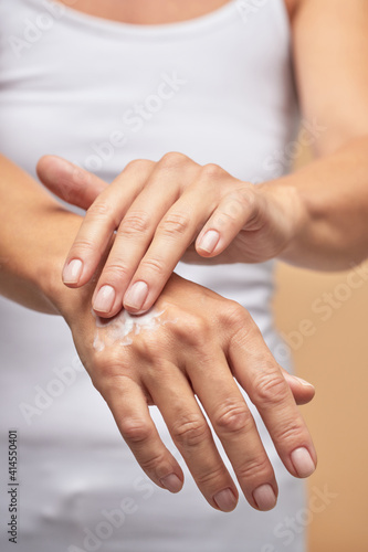 Fototapeta Naklejka Na Ścianę i Meble -  For dry skin. Vertical shot of a woman rubbing moisturizer on hands on beige background
