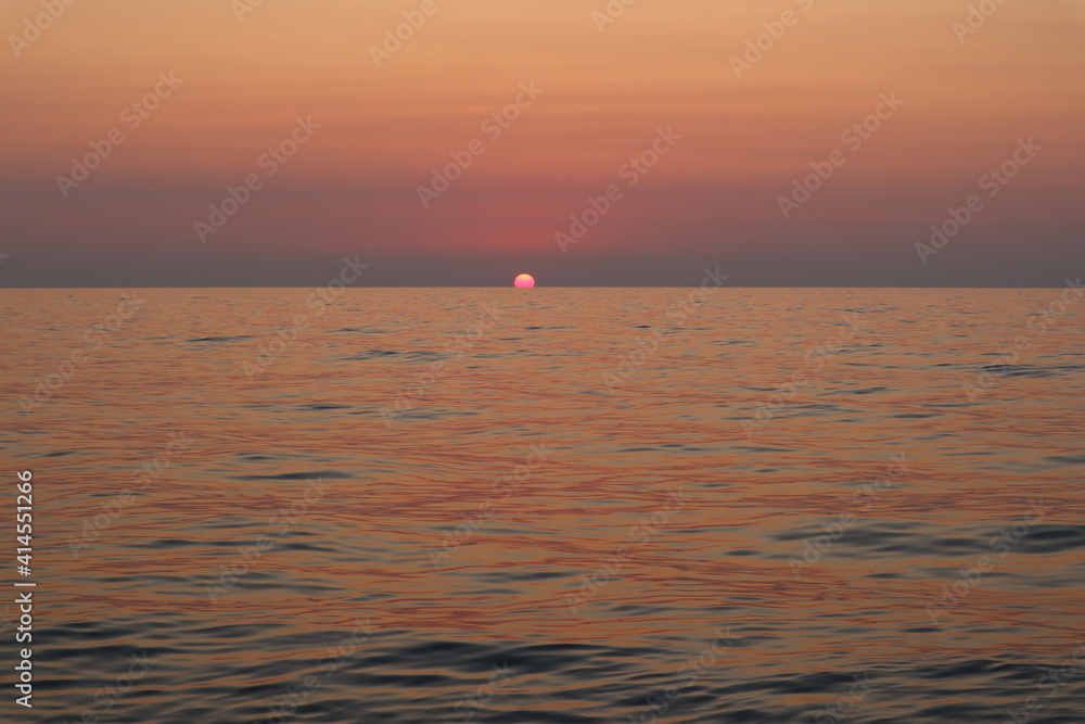 Seascape sunset on the coast of Italy, the sun disc is hidden behind the horizon. Delicate pink lilac sunset sky and sea in pastel colors, sun and clouds on the horizon on a quiet summer evening