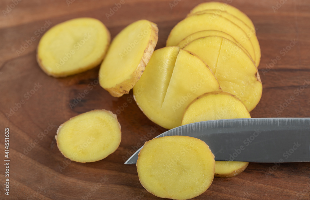 Sliced potato and knife on brown wooden board