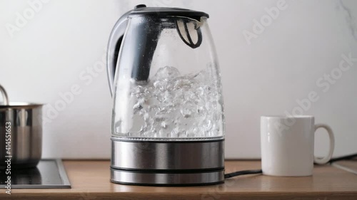 Bubbles in hot water boiling inside glass teapot in bright sunlight on the kitchen. Close-up of boiling water in transparent kettle.