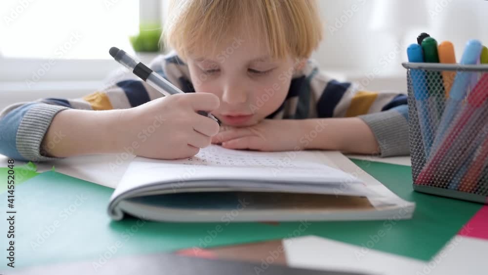 Elementary student boy doing math homework at home.Child learning to count, solves arithmetic examples, doing exercises in workbook. Preparing preschooler for school.Education for kids.Focus on hand Elementary student boy doing math homework at home.Child learning to count, solves arithmetic examples, doing exercises in workbook. Preparing preschooler for school.Education for kids.Focus on hand