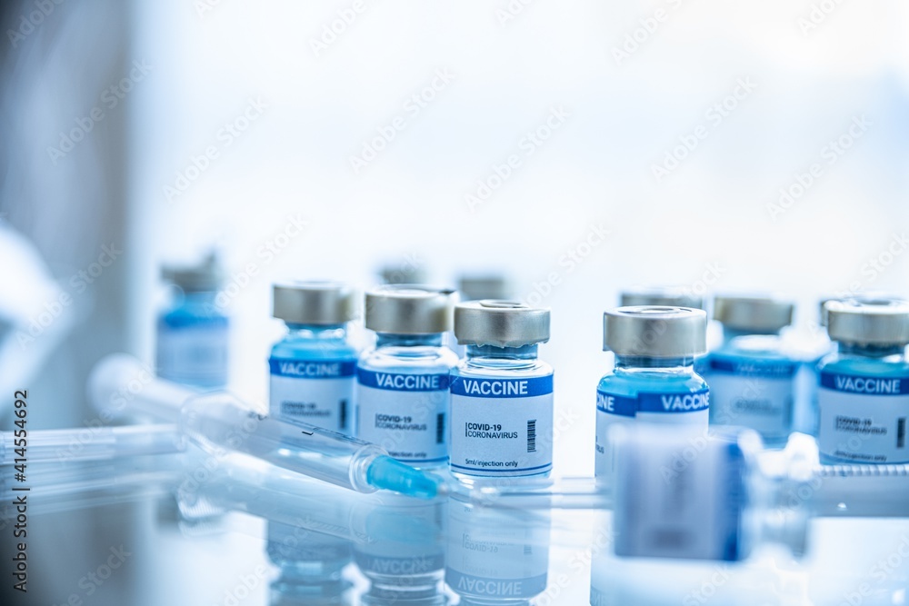 Vials, ampoules with coronavirus vaccine and syringe on laboratory bench. Fight the coronavirus.