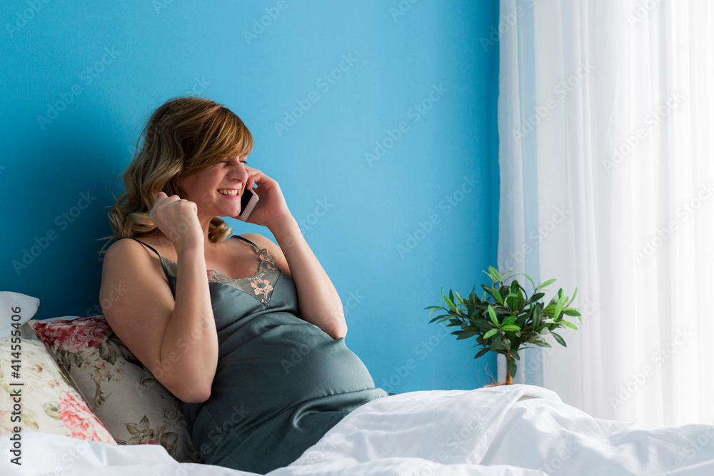 A pregnant woman in a semi-sitting position talking over her phone excited by the news. A pregnant woman in a semi-sitting position talking over her phone excited by the news.