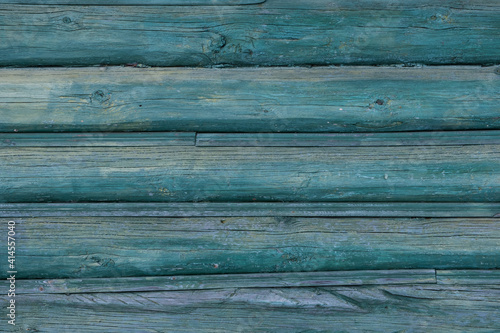 An old wall of pine logs. Weathered, faded wood. Green paint faded in the sun. Factura of a tree.