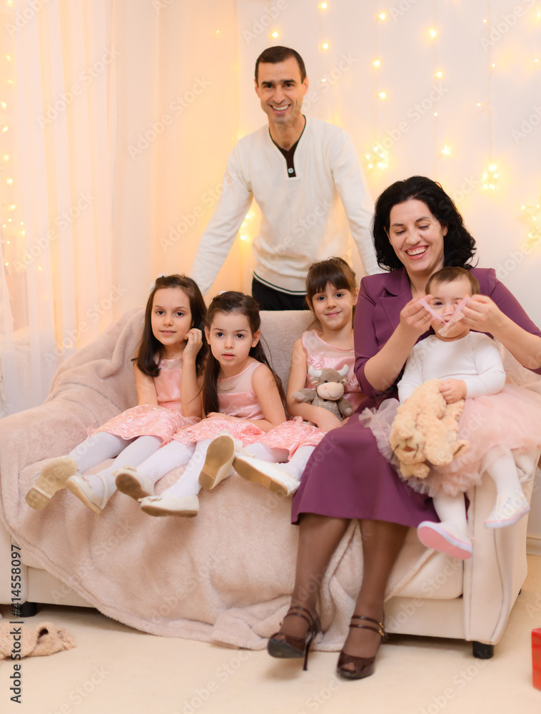 family portrait of a parents and children, sitting on a couch in home interior decorated with lights and gifts family portrait of a parents and children, sitting on a couch in home interior decorated with lights and gifts