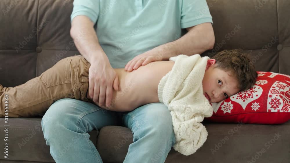 father gives his son a back massage by putting him on his lap. A parent massages the child's back while sitting on the couch at home. father gives his son a back massage by putting him on his lap. A parent massages the child's back while sitting on the couch at home.