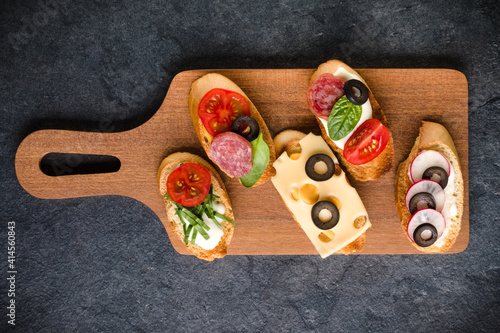Open faced sandwich canape or crostini on a wooden serving board on dark stone  background closeup. Top view.