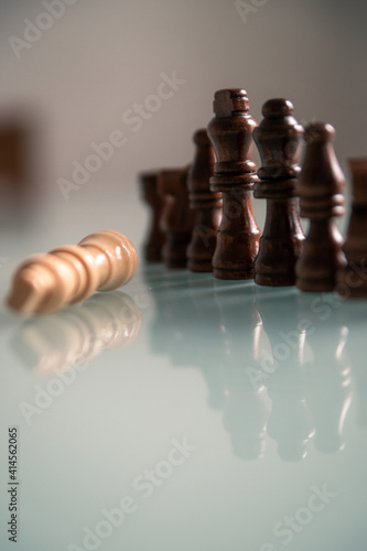 Chess pieces lined up on a table white and black with fallen king representing defeat