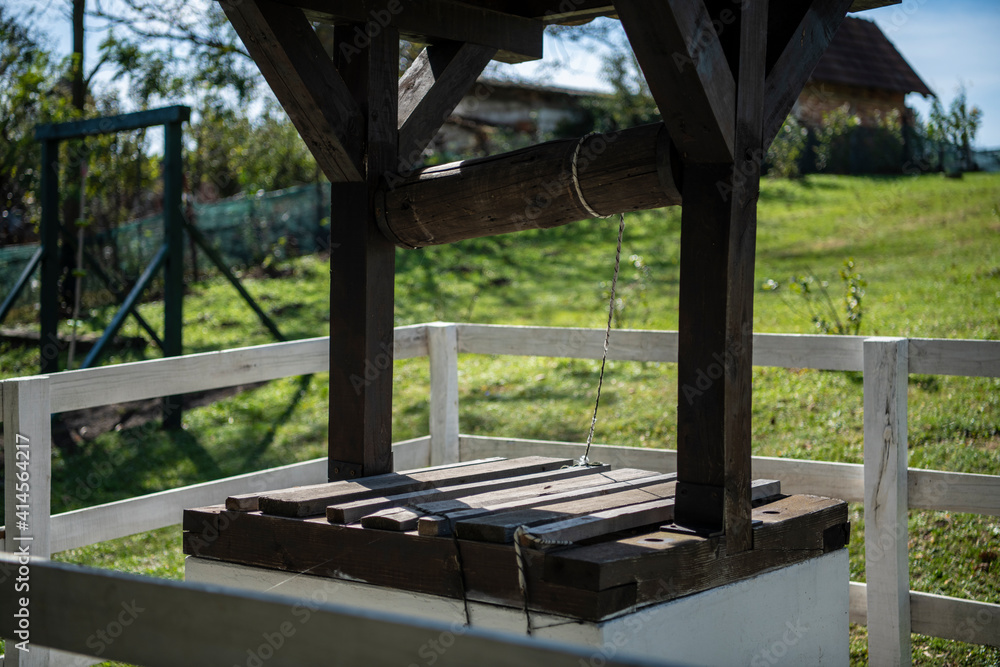 Old wooden draw water well in the countryside, in Serbian Village with white fence and grassland in background. Old wooden draw water well in the countryside, in Serbian Village with white fence and grassland in background.