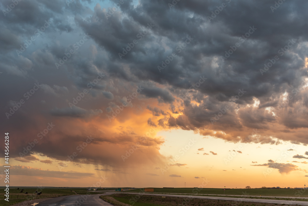 A flat landscape highway seen before a cloudy storm approaching with pink, orange dark clouds, shining sun and dark country, rural land below. Great for sky replacement for editing photos or drawing. 
