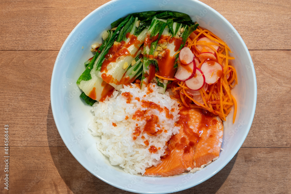 Homemade Salmon and Rice with Pickled Vegetables and Spicy Korean Red Pepper Gochujang Source Served in White Large Bowl on Wooden Table