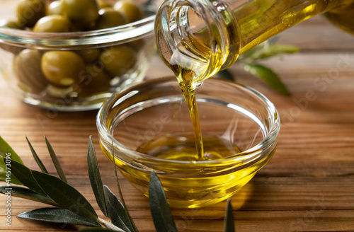 Pour olive oil into a glass bowl set against a wooden background