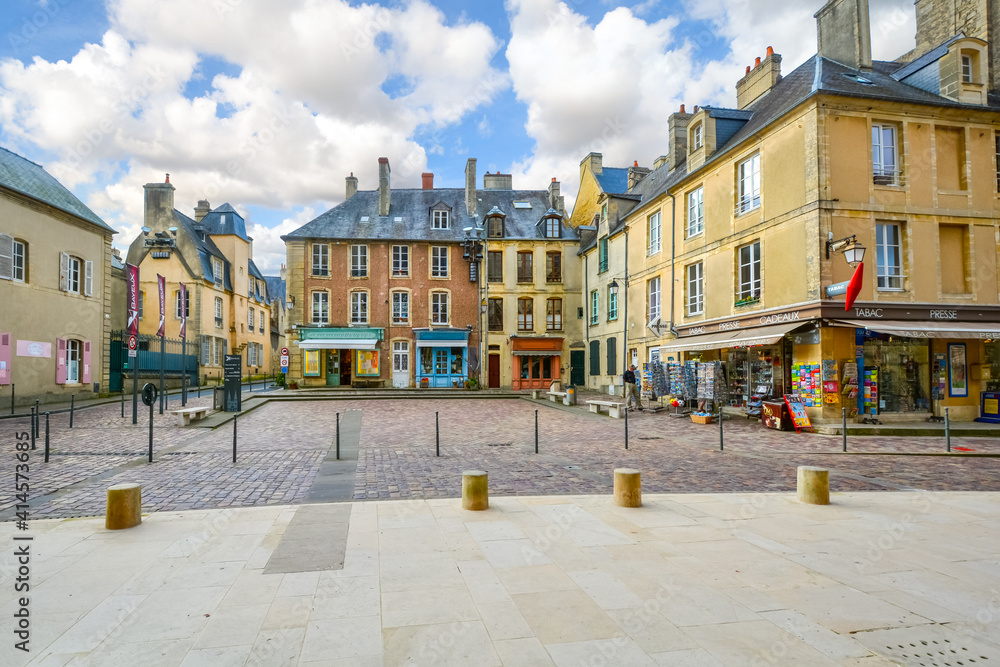 The small square outside the entrance to the Bayeux Cathedral, with colorful shops and cafes in the Normandy town of Bayeux, France.