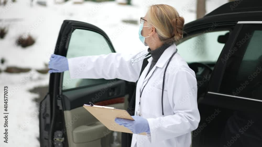 Closeup of mature woman doctor or nurse wearing face mask and gloves getting out of car, making a house call home visit in a rural area. Closeup of mature woman doctor or nurse wearing face mask and gloves getting out of car, making a house call home visit in a rural area.
