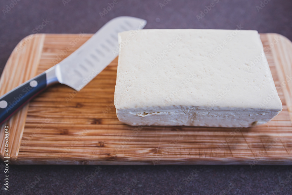 simple food ingredients, block of extra firm tofu on cutting board with knife