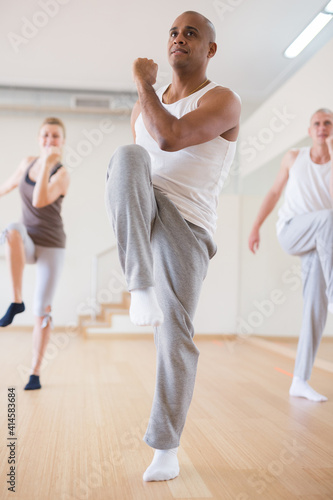 Group of happy adult people enjoying active dance in modern studio. Focus on expressive Hispanic man