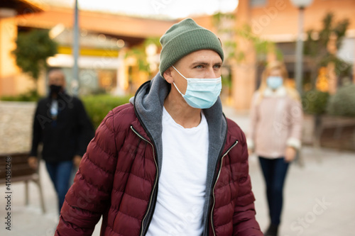 Portrait of young adult man wearing face mask for viral or pollution protection walking at cold sunny day
