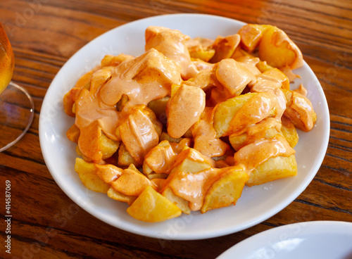 Top view of Patatas bravas, traditional Spanish dish of fried potatoes served with cheese sauce and spicy sauce with paprika