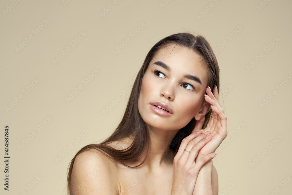Brunette with bare shoulders close-up long hair beige background clean skin Brunette with bare shoulders close-up long hair beige background clean skin