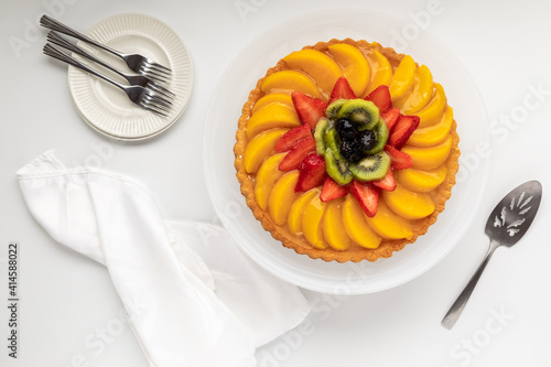 Top down view of a German fruit flan including peaches, strawberries and kiwi.