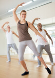 Portrait of smiling young woman practicing ballet dance moves during group class in choreographic studio